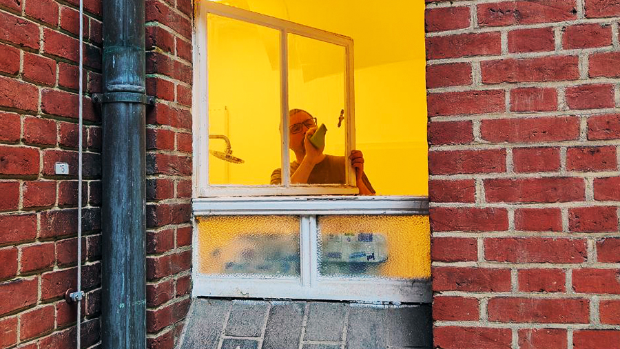 Person putzt altes Fenster in Backsteinwand