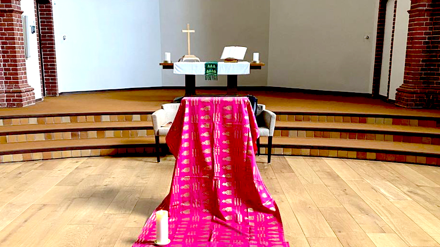 Vor dem Altar mit Kerzen und Bibel stehen 2 Sessel, über die ein pinkes Tuch gespannt ist. Am Boden steht eine Kerze.