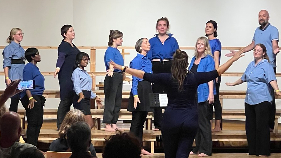 Chor mit blauen Shirts steht auf Bühne und singt.